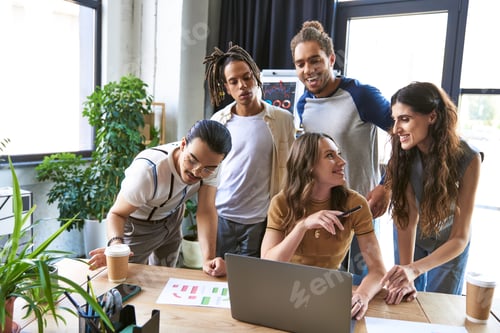 Preview: creative multicultural team sharing ideas at work desk with laptop, graphs and coffee to go