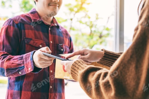 Preview: woman receiving parcel box and signing name on the phone from delivery man at the house's door