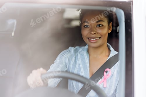 Preview: Beautiful African American woman with pink cancer ribbon on chest sitting in her car