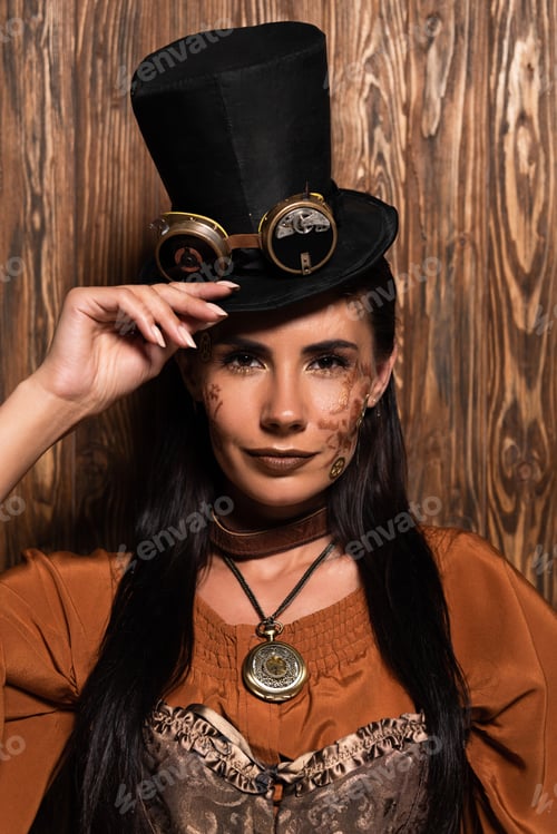 Preview: front view of steampunk woman touching top hat with goggles looking at camera on wooden
