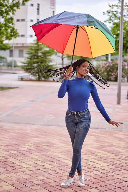 Preview: African American woman holding a colorful umbrella standing outdoors on the street.