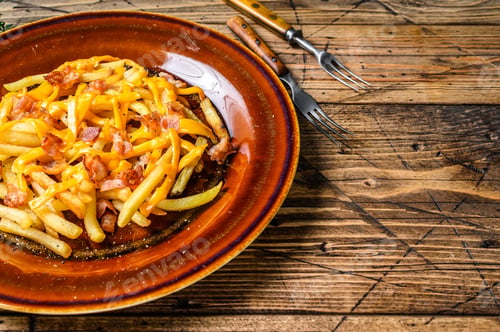 Preview: French fries with melted cheddar cheese and bacon served in a rustic plate.