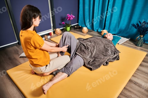 Preview: Masseuse making thai yoga massage. Woman therapist doing traditional massage treatment for patient.