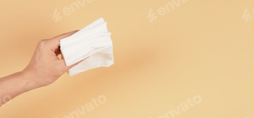 Preview: The hand is holding a small size of white paper tissues on a creamy ivory color background.