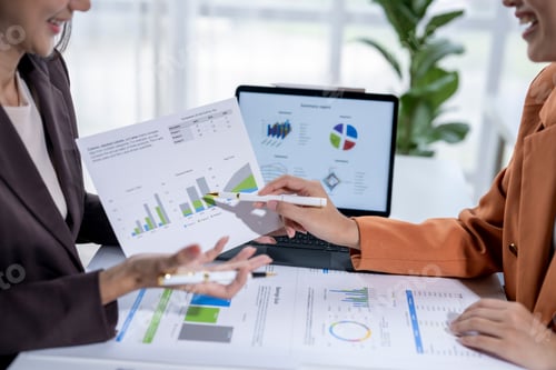 Preview: Two businesswomen analyzing financial charts and graphs on a desk