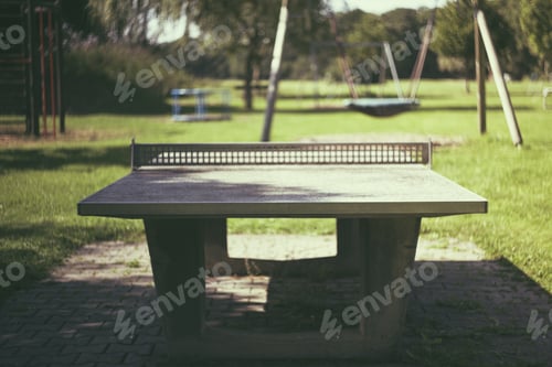 Preview: Stone tennis table in the park with a playground in the background on a sunny day