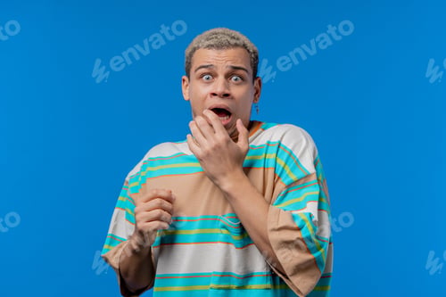 Preview: Frightened shocked man afraid of something looks into camera with big eyes full of horror on blue