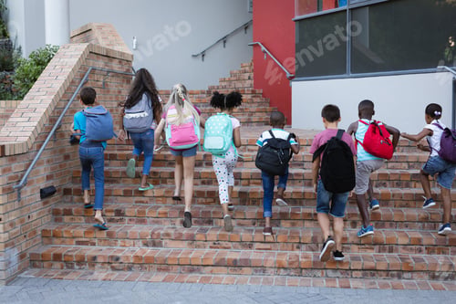 Preview: Rear view of group of diverse students with backpacks climbing up the stairs together at school
