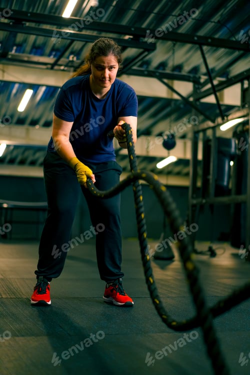 Preview: concentrated female athlete doing exercises with ropes in gym training muscles sport concept