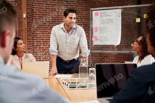 Preview: Mature Businessman Standing And Leading Office Meeting Around Table