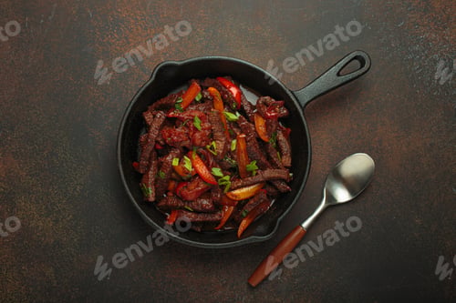 Preview: Lomo saltado, beef and red pepper stir fry cooking in cast iron pan, traditional Peruvian dish