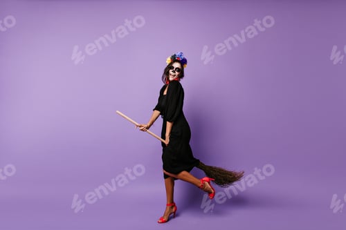 Preview: Full-length portrait of dead bride dancing in halloween. Excited brunette witch sitting on broom.