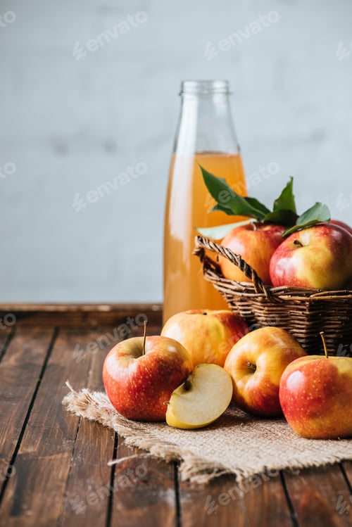 Preview: close up view of glass bottle of apple juice and apples in basket on wooden tabletop