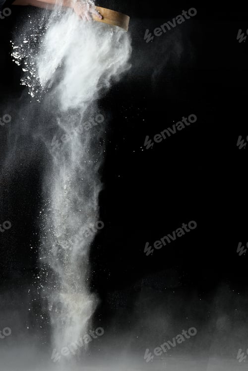 Preview: Female hand sifts white wheat flour through a round wooden sieve on a black background