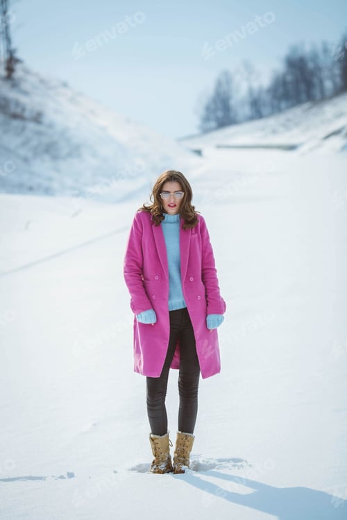 Preview: Attractive brunette female in glasses and a cute pink coat posing for the camera on a winter day