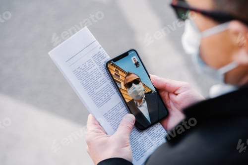 Preview: Man makes video call via modern cellphone, wears protective medical mask during virus spreading