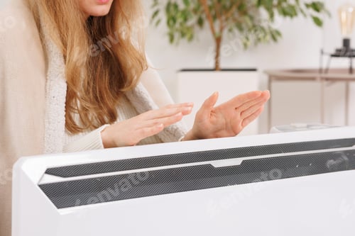Preview: Frozen young woman with plaid warming near radiator at home