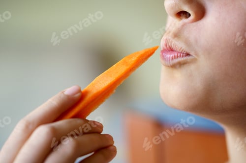 Preview: Anonymous girl puckering lips while holding fresh carrot slice