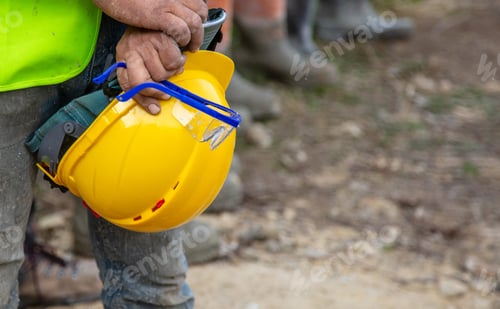 Preview: Worker holding yellow safety helmet and goggles at construction site outdoors