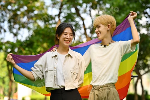 Preview: Male and female LGBT friends holding and raising a rainbow flag.
