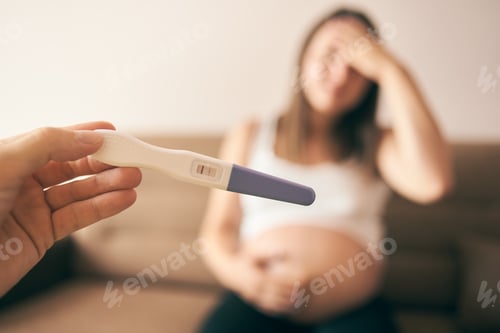 Preview: Selective focus of pregnancy test and sad lady at background