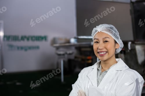 Preview: Woman standing, smiling with crossed arms in food processing plant, lab coat, hair net, copy space