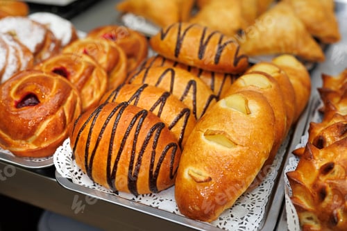 Preview: Freshly baked pastries with chocolate drizzle and fruit filling on a tray.