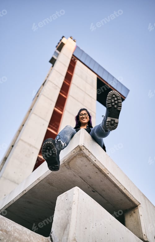 Preview: young latin woman wearing glasses blue pants sitting smiling at camera with hand hand out calm and