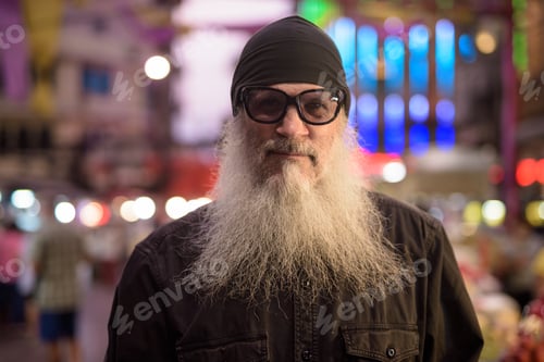 Preview: Face of mature bearded tourist man wearing sunglasses in Chinatown at night