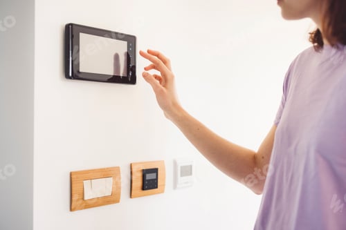 Preview: Young unrecognizable caucasian woman answering the door bell on modern home security device with a s