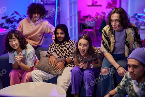Preview: Large group of happy young friends watching broadcast at home party