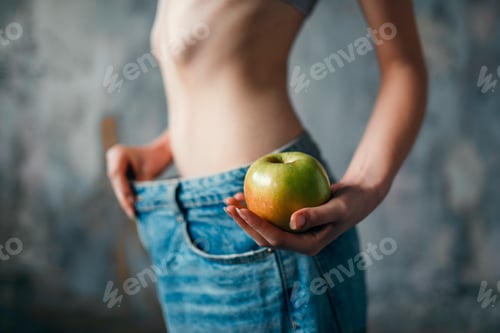Preview: Woman with apple in hand tries on big size jeans