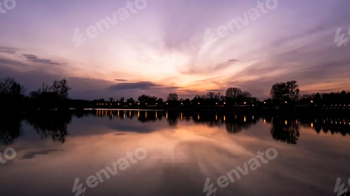 Preview: Sunset over a lake with street lights reflecting in the water. Purple hues of the sky and clouds.
