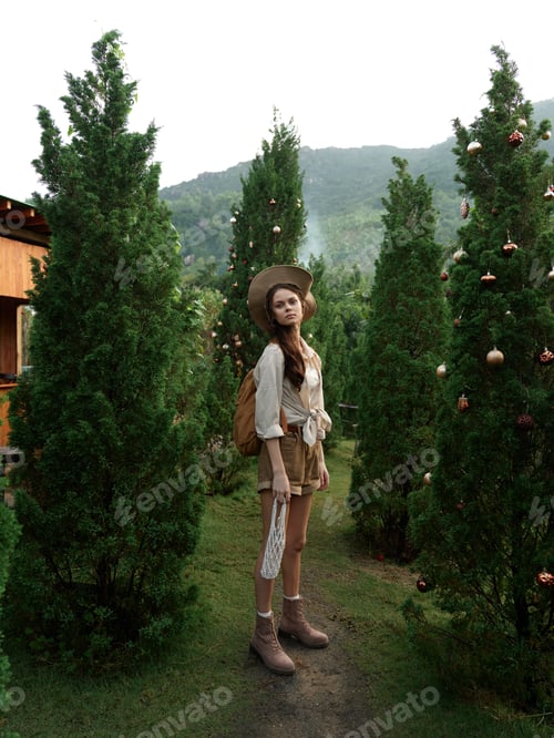 Preview: A woman wearing a hat and carrying a backpack on a path next to a forest of evergreen trees