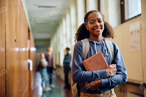 Preview: Happy black teenage girl in high school hallway looking at camera.