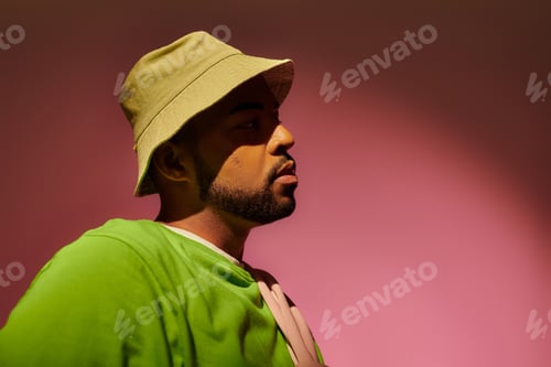 Preview: stylish young male model with beard in panama posing in profile on pink background, fashion concept