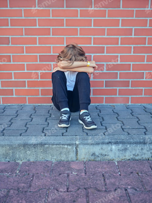 Preview: Unrecognizable boy hugging knees and sitting near brick wall