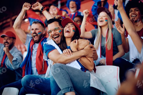 Preview: Group of cheerful sports fans celebrating while spectating game from stadium stands.