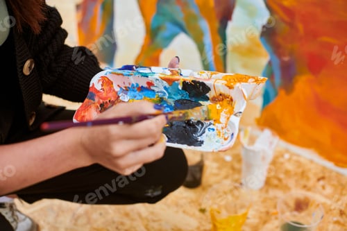 Preview: Female painter hand dips paintbrush into palette of colorful paints for live painting of picture
