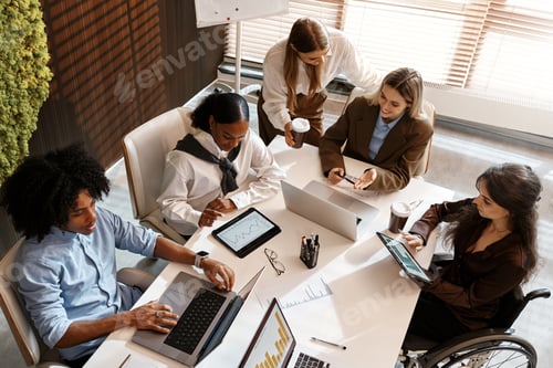 Preview: Diverse business team analyzing charts during office meeting from top view