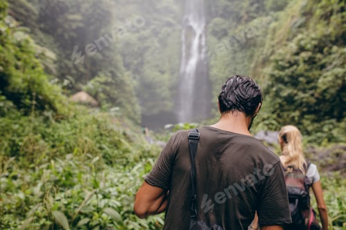Preview: Couple of tourists walking towards a waterfall in forest