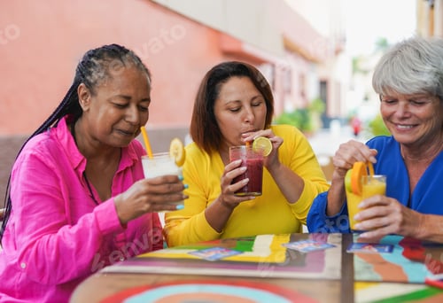 Preview: Happy multiracial senior women meeting in the city while drinking smoothie at bar terrace