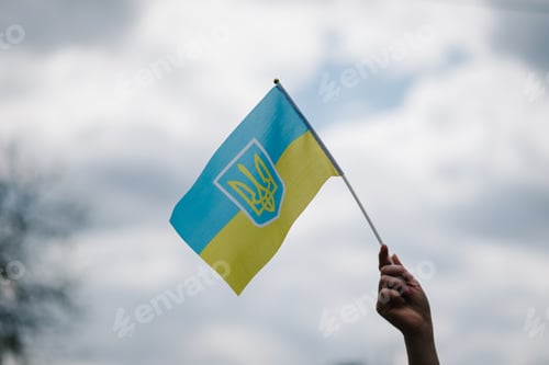 Preview: Ukrainian yellow and blue flag flutters in wind against the sky. A woman hand holds a flag