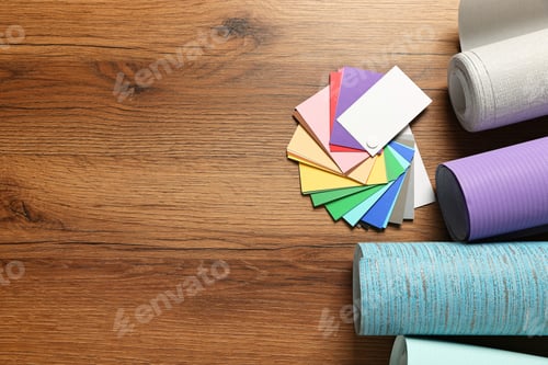 Preview: Different wallpaper rolls and color palette samples on wooden table, flat lay. Space for text