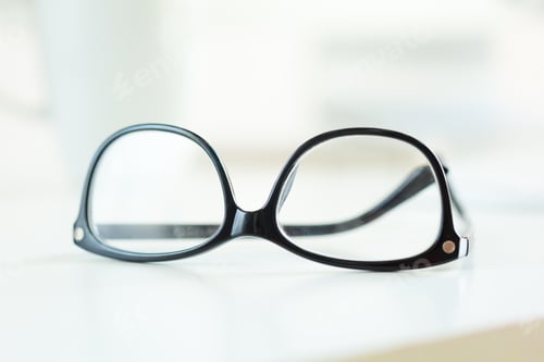 Preview: Glasses resting on a table with a blurred background and bright light