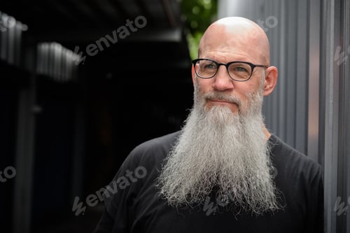 Preview: Mature handsome bald bearded man with eyeglasses thinking in the streets outdoors