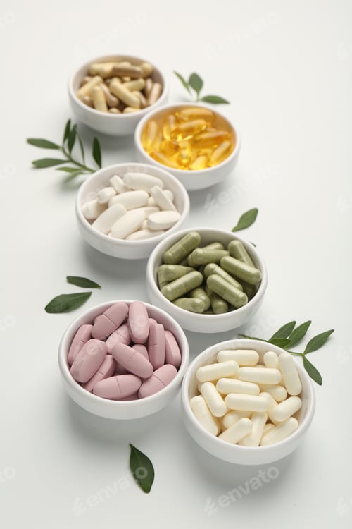 Preview: Different vitamin capsules in bowls and leaves on white background