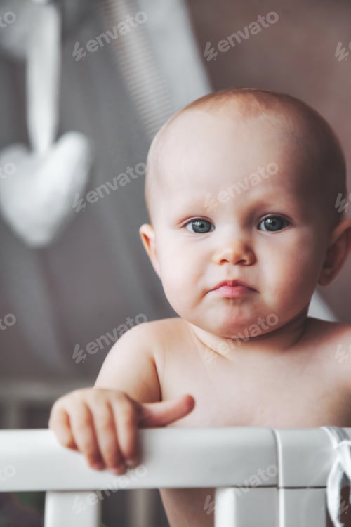 Preview: Portrait of serious adorable baby looking at camera from his infant cot