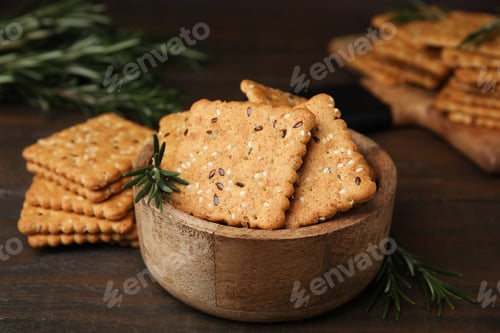 Preview: Cereal crackers with flax, sesame seeds and rosemary in bowl on wooden table, closeup