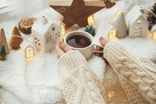 Preview: Cozy winter. Hands in sweater holding stylish cup of tea with modern christmas decoration